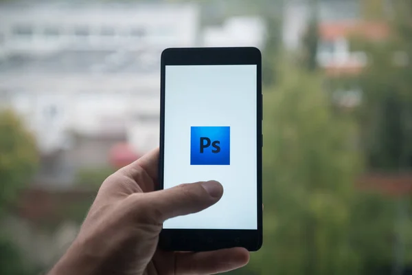 Hombre sosteniendo el teléfono inteligente con el logotipo de Adobe Photoshop con el dedo en la pantalla . —  Fotos de Stock