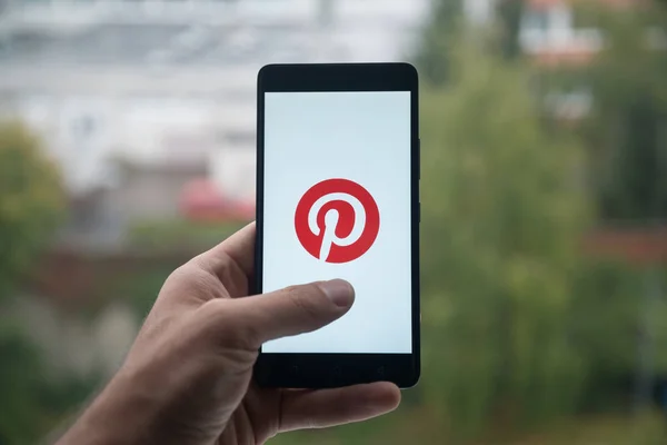 Hombre sosteniendo el smartphone con el logotipo de Pinterest con el dedo en la pantalla . —  Fotos de Stock