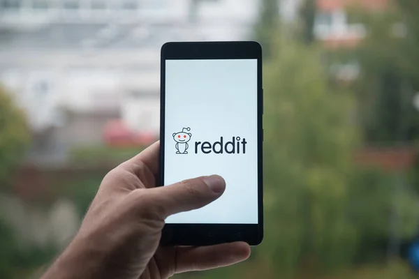 Man met smartphone met Reddit logo met de vinger op het scherm. — Stockfoto