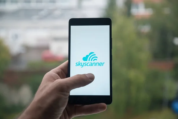 Człowiek posiadający smartfon z logo Skyscanner z palca na ekranie. — Zdjęcie stockowe