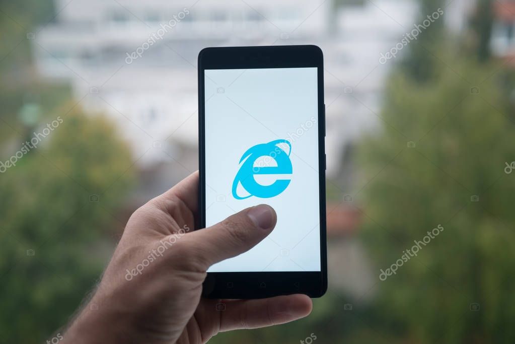London, United Kingdom, october 3, 2017: Man holding smartphone with Internet explorer logo with the finger on the screen.