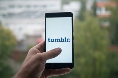 Üstünde belgili tanımlık perde smartphone parmaklı Tumblr logolu tutan adam.
