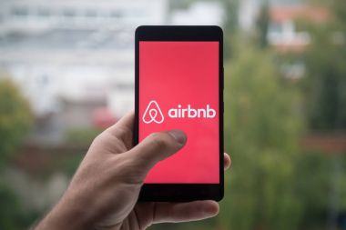Üstünde belgili tanımlık perde smartphone ile parmak Airbnb logolu tutan adam.