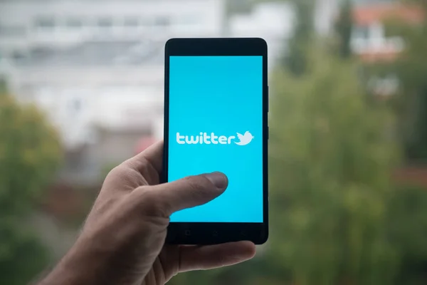 Homem segurando smartphone com logotipo do Twitter com o dedo na tela . — Fotografia de Stock