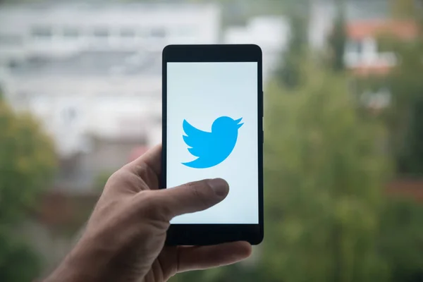 Homem segurando smartphone com logotipo do Twitter com o dedo na tela . — Fotografia de Stock