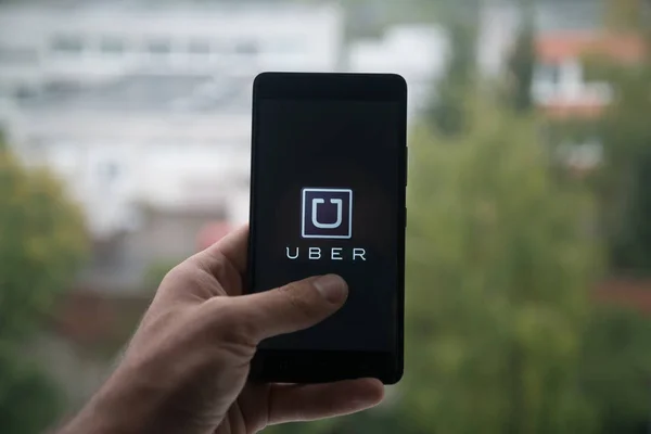 Hombre sosteniendo el teléfono inteligente con el logotipo de Uber con el dedo en la pantalla . — Foto de Stock