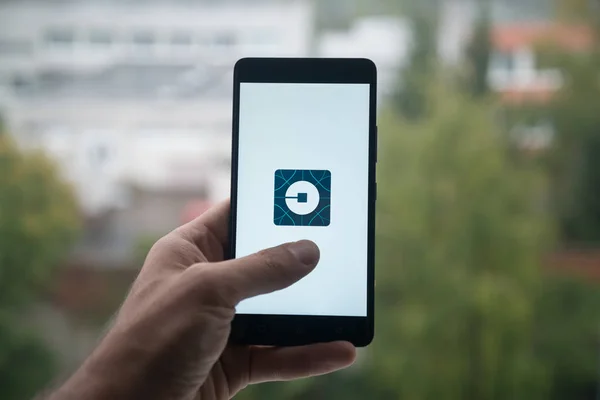 Hombre sosteniendo el teléfono inteligente con el logotipo de Uber con el dedo en la pantalla . —  Fotos de Stock