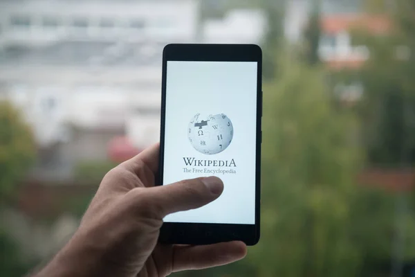 Muž, který držel smartphone s logem Wikipedie s prstem na obrazovce. — Stock fotografie