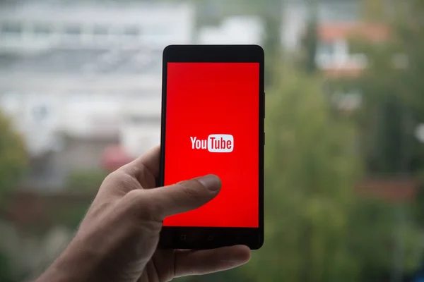 Üstünde belgili tanımlık perde smartphone parmak ile Youtube logolu tutan adam. — Stok fotoğraf