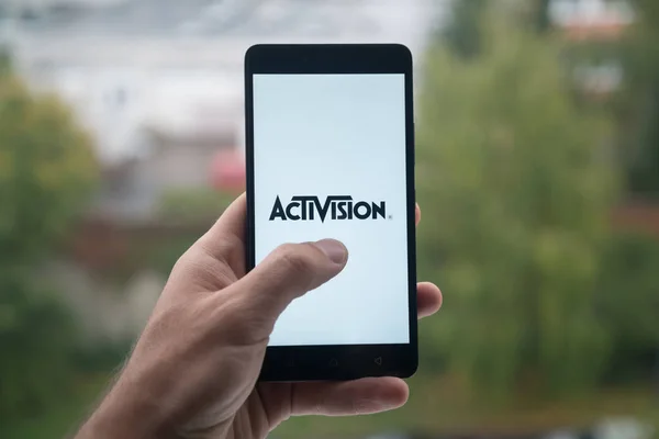 Człowiek posiadający smartfon z logiem Activision z palca na ekranie. — Zdjęcie stockowe