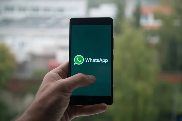 Hombre sosteniendo el teléfono inteligente con el logotipo de Whatsapp con el dedo en la pantalla . — Foto de Stock