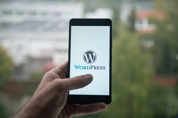 Hombre sosteniendo el teléfono inteligente con logotipo de Wordpress con el dedo en la pantalla . — Foto de Stock