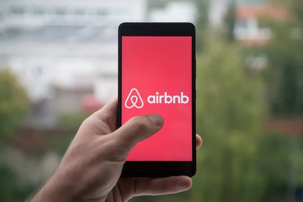 Hombre sosteniendo teléfono inteligente con el logotipo de Airbnb con el dedo en la pantalla . — Foto de Stock