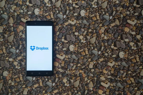 Logotipo de Dropbox en el teléfono inteligente en el fondo de piedras pequeñas — Foto de Stock