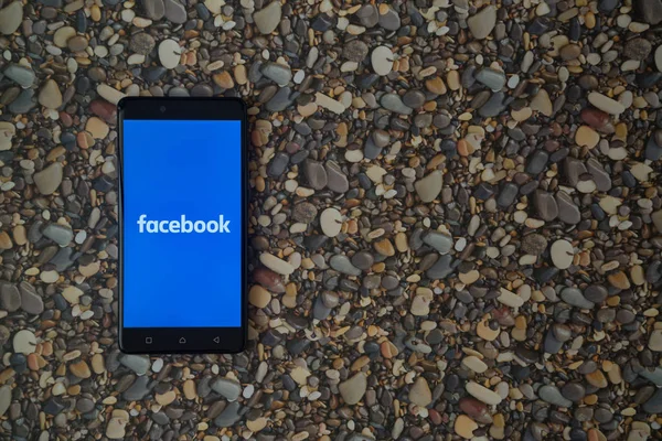 Logo de Facebook en el teléfono inteligente en el fondo de piedras pequeñas — Foto de Stock