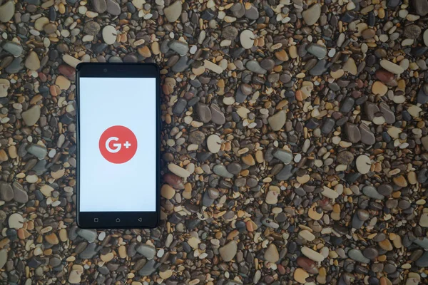 Google plus logotipo no smartphone no fundo de pequenas pedras — Fotografia de Stock
