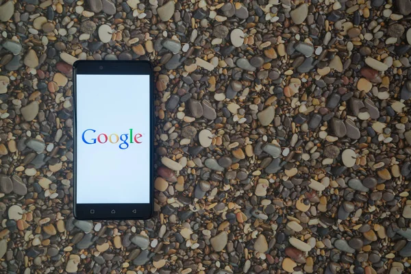 Logotipo de Google en el teléfono inteligente en el fondo de piedras pequeñas — Foto de Stock