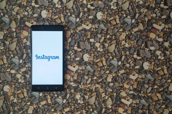 Logo de Instagram en el teléfono inteligente en el fondo de piedras pequeñas — Foto de Stock