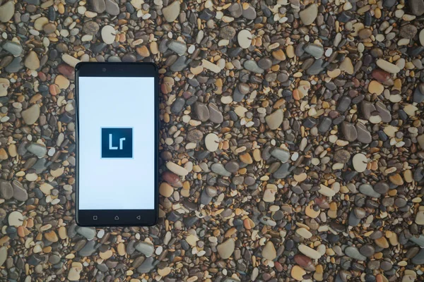 Adobe Photoshop logotipo lightroom en el teléfono inteligente en el fondo de piedras pequeñas — Foto de Stock