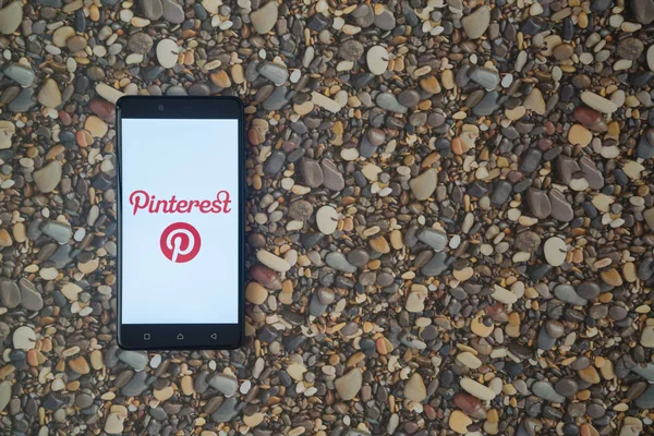 Logotipo de Pinterest en el smartphone sobre fondo de piedras pequeñas — Foto de Stock