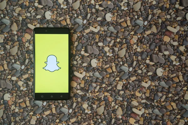 Logotipo Snapchat en el teléfono inteligente en el fondo de piedras pequeñas — Foto de Stock