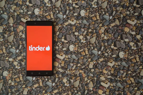 Tinder logo op smartphone op achtergrond van kleine stenen — Stockfoto