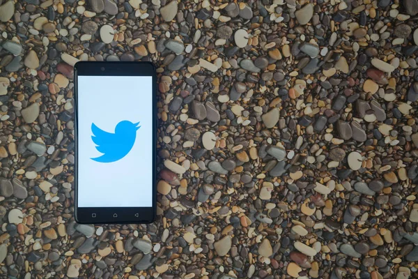 Logotipo de Twiitter en el teléfono inteligente en el fondo de piedras pequeñas — Foto de Stock