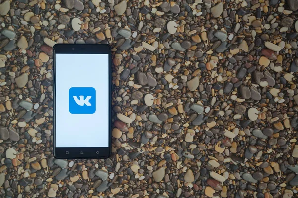 Logotipo Vkontakte no smartphone no fundo de pequenas pedras — Fotografia de Stock