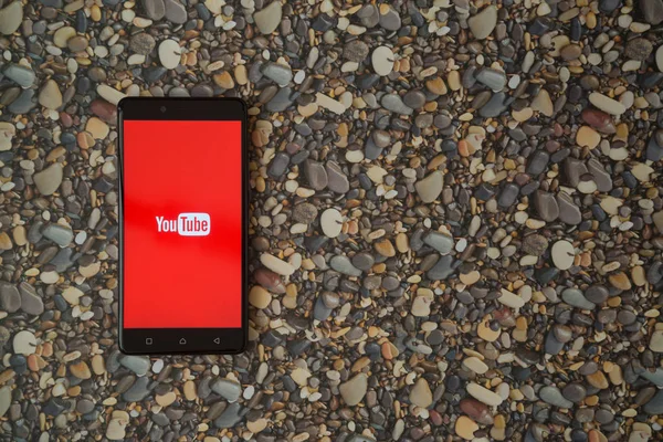 Logotipo de Youtube en el teléfono inteligente sobre fondo de piedras pequeñas — Foto de Stock