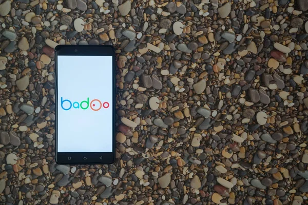 Logotipo de Badoo en el teléfono inteligente sobre fondo de piedras pequeñas — Foto de Stock