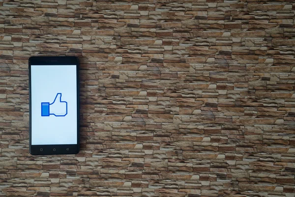 Logotipo de Facebook pulgar hacia arriba en la pantalla del teléfono inteligente sobre fondo de piedra — Foto de Stock