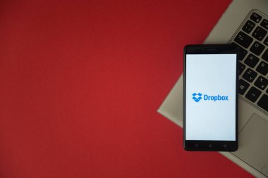 Dropbox logo on smartphone screen placed on laptop keyboard.  clipart