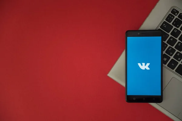 Logotipo de Vkontakte en la pantalla del teléfono inteligente colocado en el teclado portátil . — Foto de Stock