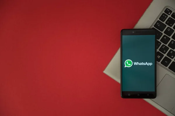 Logo WhatsApp na ekran smartfona umieszczone na klawiaturze laptopa. — Zdjęcie stockowe