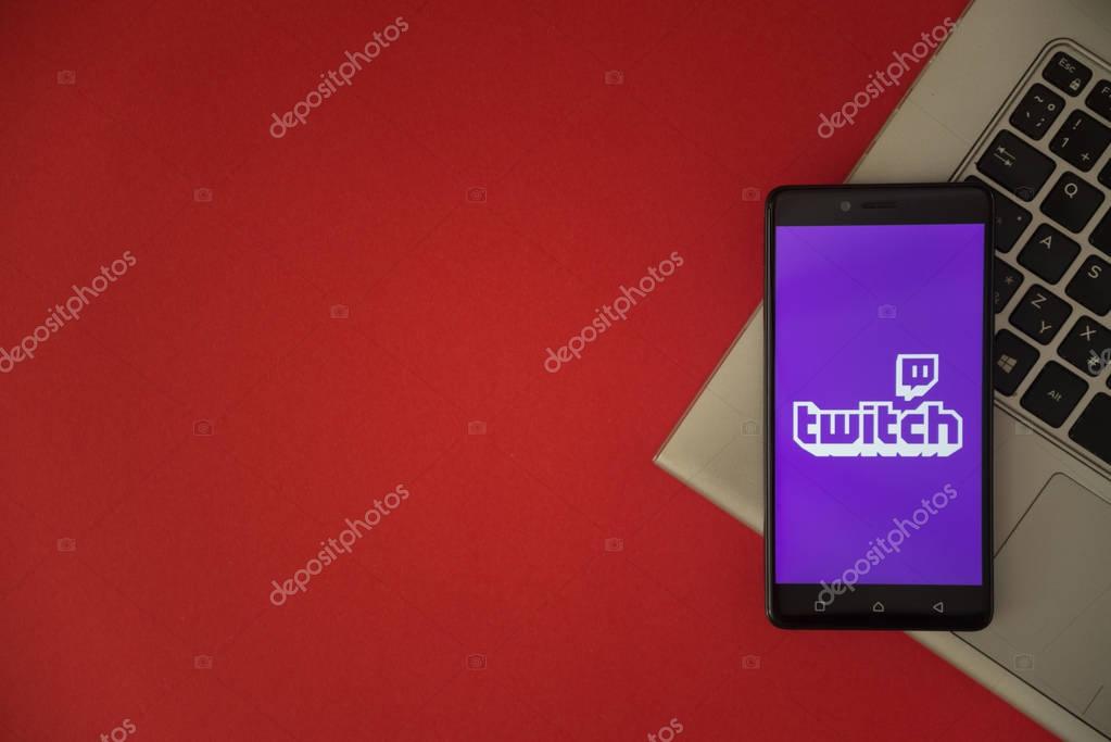 London, United Kingdom, October 23, 2017: Twitch logo on smartphone screen placed on laptop keyboard. Empty place to write information with red background.