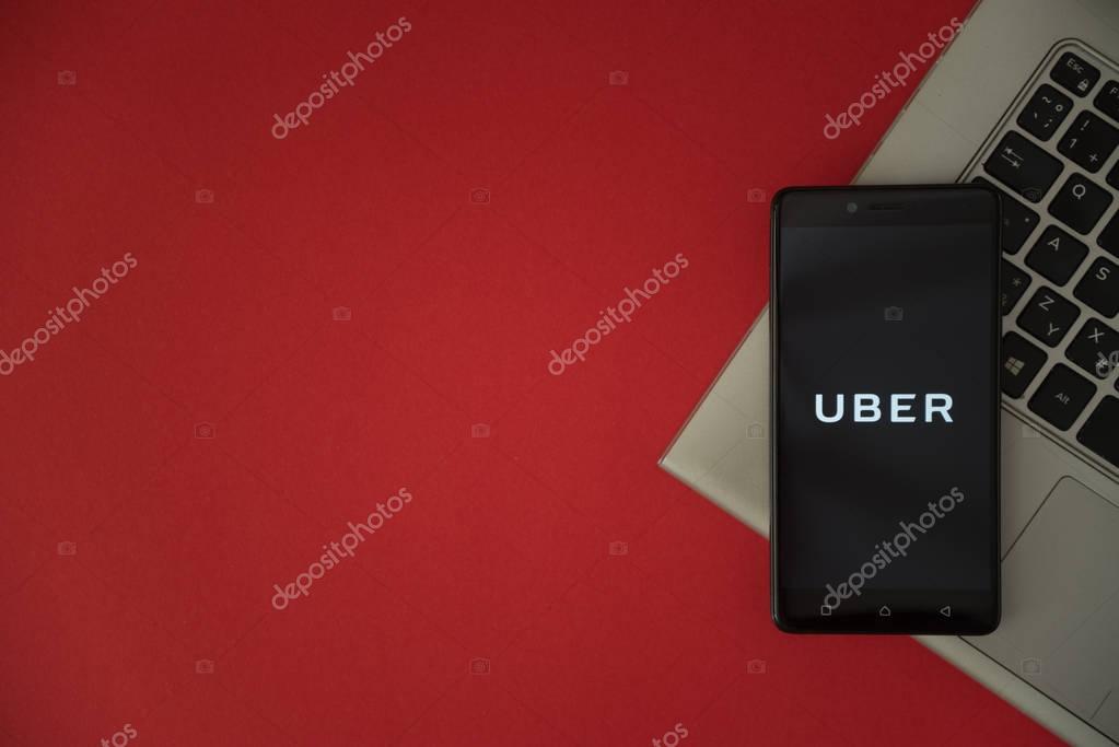 London, United Kingdom, October 23, 2017: Uber logo on smartphone screen placed on laptop keyboard. Empty place to write information with red background.
