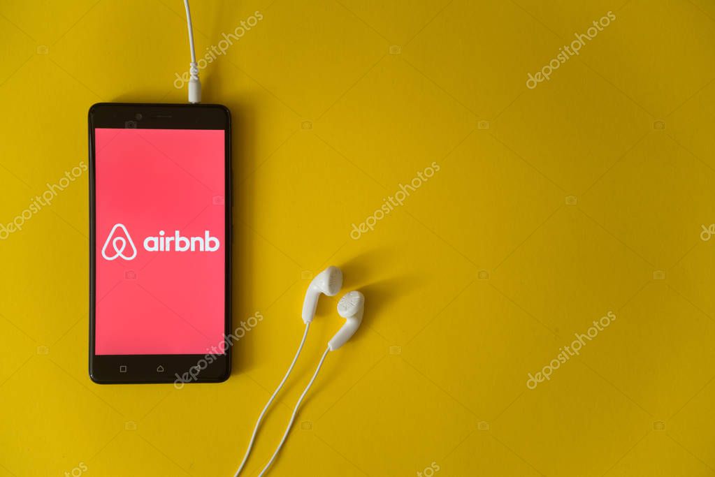 Los Angeles, USA, october 23, 2017: Airbnb logo on smartphone screen and earphones plugged in on yellow background.