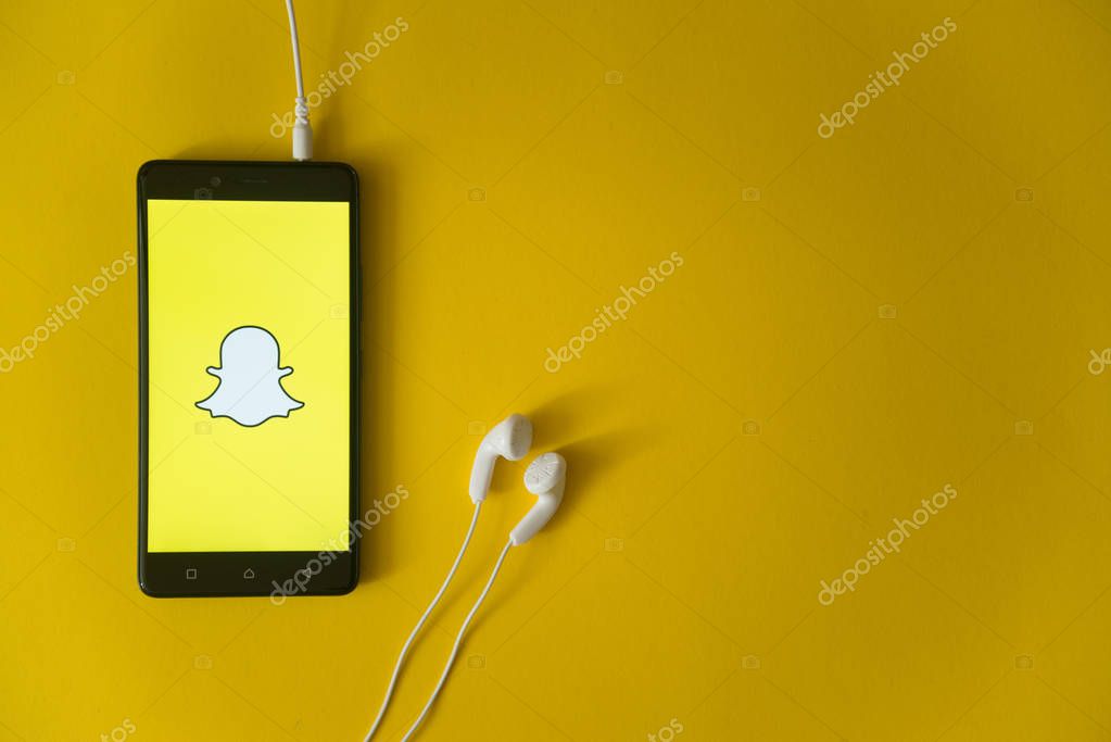 Los Angeles, USA, october 23, 2017: Snapchat logo on smartphone screen and earphones plugged in on yellow background.