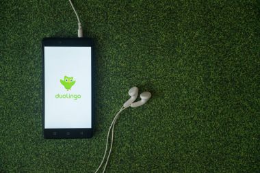 Duolingo logo üstünde smartphone perde yeşil çim zemin üzerine.