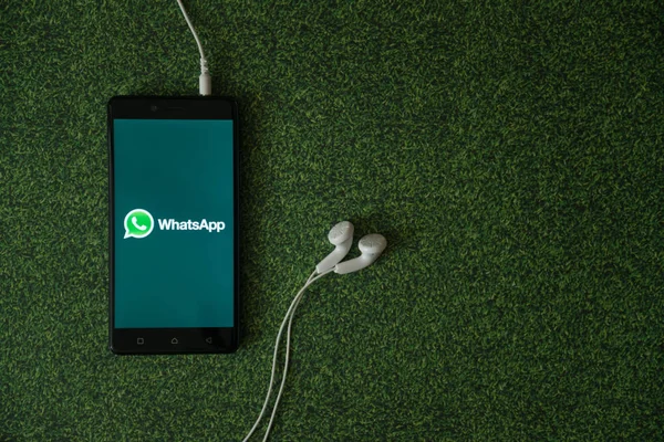 WhatsApp logo na obrazovku smartphonu na zelené trávě pozadí. — Stock fotografie