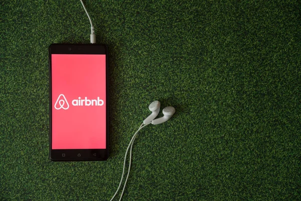 Airbnb logo on smartphone screen on green grass background. — Stock Photo, Image