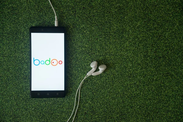 Логотип Badoo на экране смартфона на зеленом фоне травы . — стоковое фото