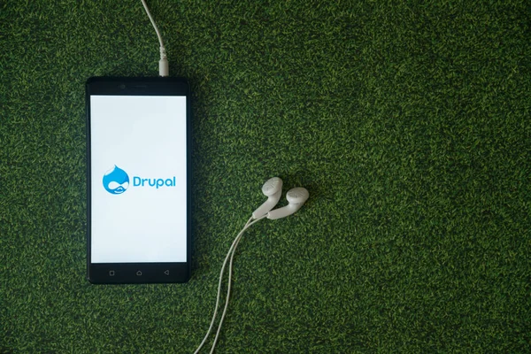 Drupal logo na ekranie smartfona na tle zielonej trawie. — Zdjęcie stockowe
