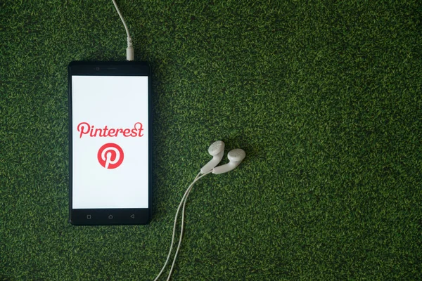 Logotipo do Pinterest na tela do smartphone no fundo da grama verde . — Fotografia de Stock