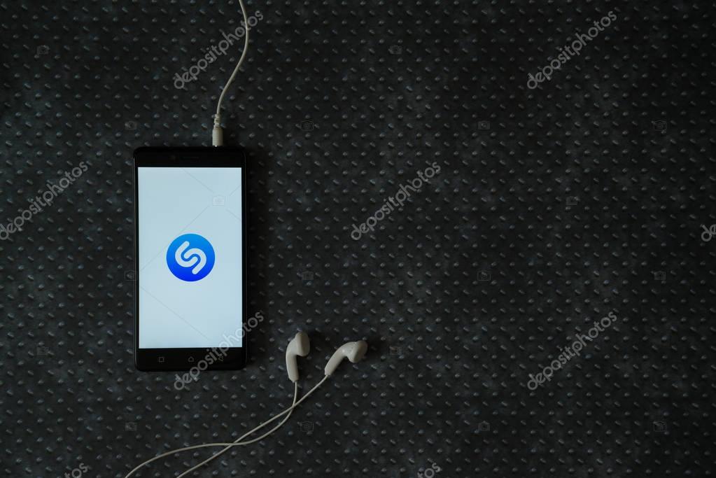 Los Angeles, USA, october 23, 2017: Shazam logo on smartphone screen and earphones plugged in on metal plate background.