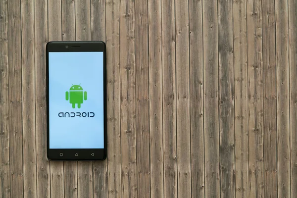 Logo de Android en la pantalla del teléfono inteligente sobre fondo de madera . — Foto de Stock