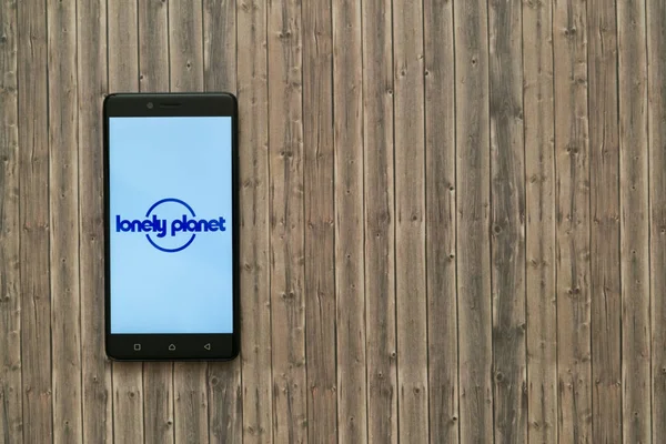 Logo Lonely planet en la pantalla del teléfono inteligente sobre fondo de madera . — Foto de Stock