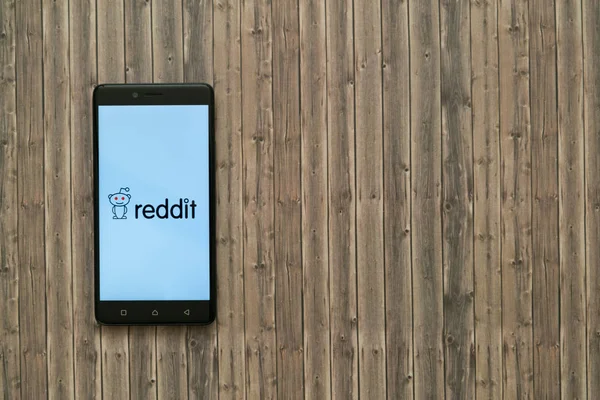 Reddit logo na obrazovku smartphonu na dřevěné pozadí. — Stock fotografie
