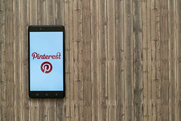 Logotipo do Pinterest na tela do smartphone no fundo de madeira . — Fotografia de Stock