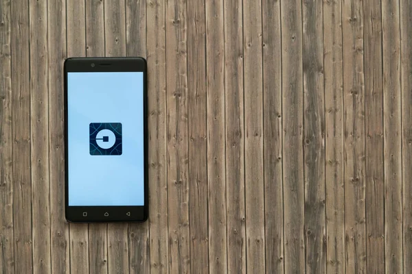 Logotipo de Uber en la pantalla del smartphone sobre fondo de madera . — Foto de Stock